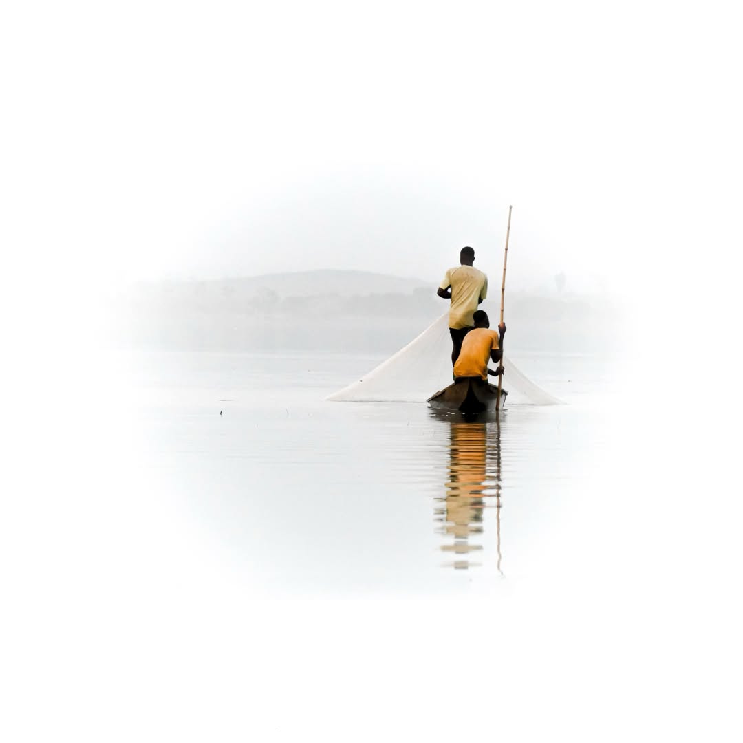 Fishermen casting a net from a wooden boat on calm misty water