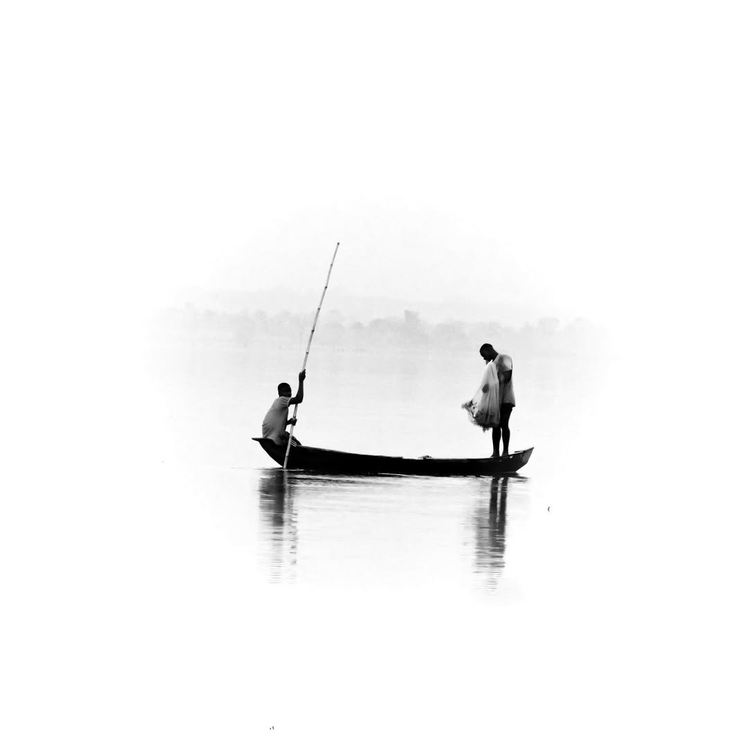 Fishermen maneuvering a boat with a long pole on misty water